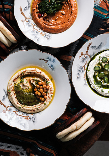 Shared dishes of hummus and dips laid out across a patterned tablecloth.